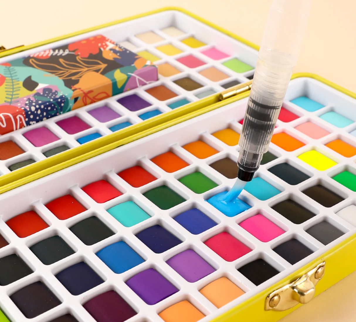 Open watercolor set featuring 100 vibrant colors with a water brush painting bright blue shade in a yellow case