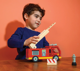 Young boy playing with a red wooden fire engine toy featuring an extendable ladder and details on a wooden table.