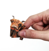 Hand holding a small origami Highland cow made from a pre-printed paper folding kit with detailed face design