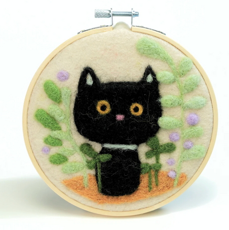Needle felted black cat surrounded by green leaves and purple flowers in wooden embroidery hoop.