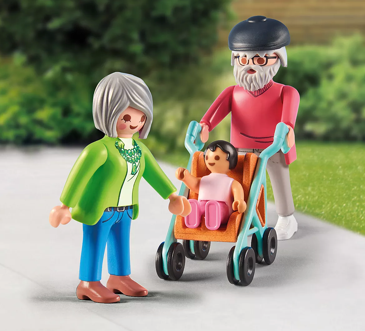Elderly couple with gray hair and glasses pushing and holding hands of a child seated in stroller outdoors