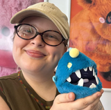 Anglerfish Snackers blue plush toy held by a smiling person