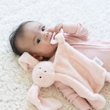 Infant lying on soft blanket holding and chewing on a soft plush bunny teether buddy toy