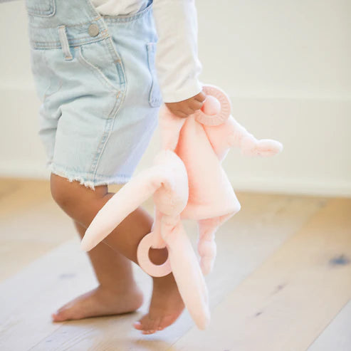 Toddler holding a soft pink bunny teether buddy with rings to soothe sore gums and a gentle rattle toy
