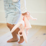 Toddler holding a soft pink bunny teether buddy with rings to soothe sore gums and a gentle rattle toy