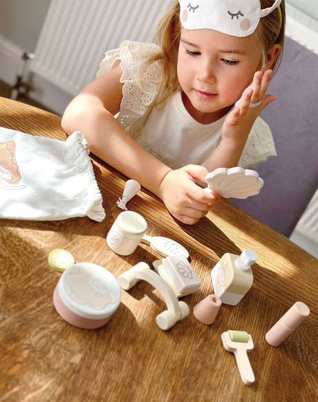 Child playing with Spa Retreat Set accessories including mirror, lotion, sugar scrub, and eye mask on wooden table.