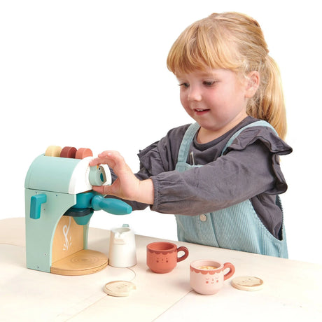 Child playing with a pastel-colored Babyccino Maker set including cups, pods, milk jug, and biscuits on a light table.