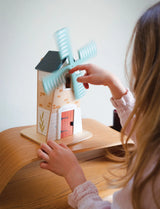 Child playing with the Penny Windmill wooden two-story toy with revolving blades on a wooden table.