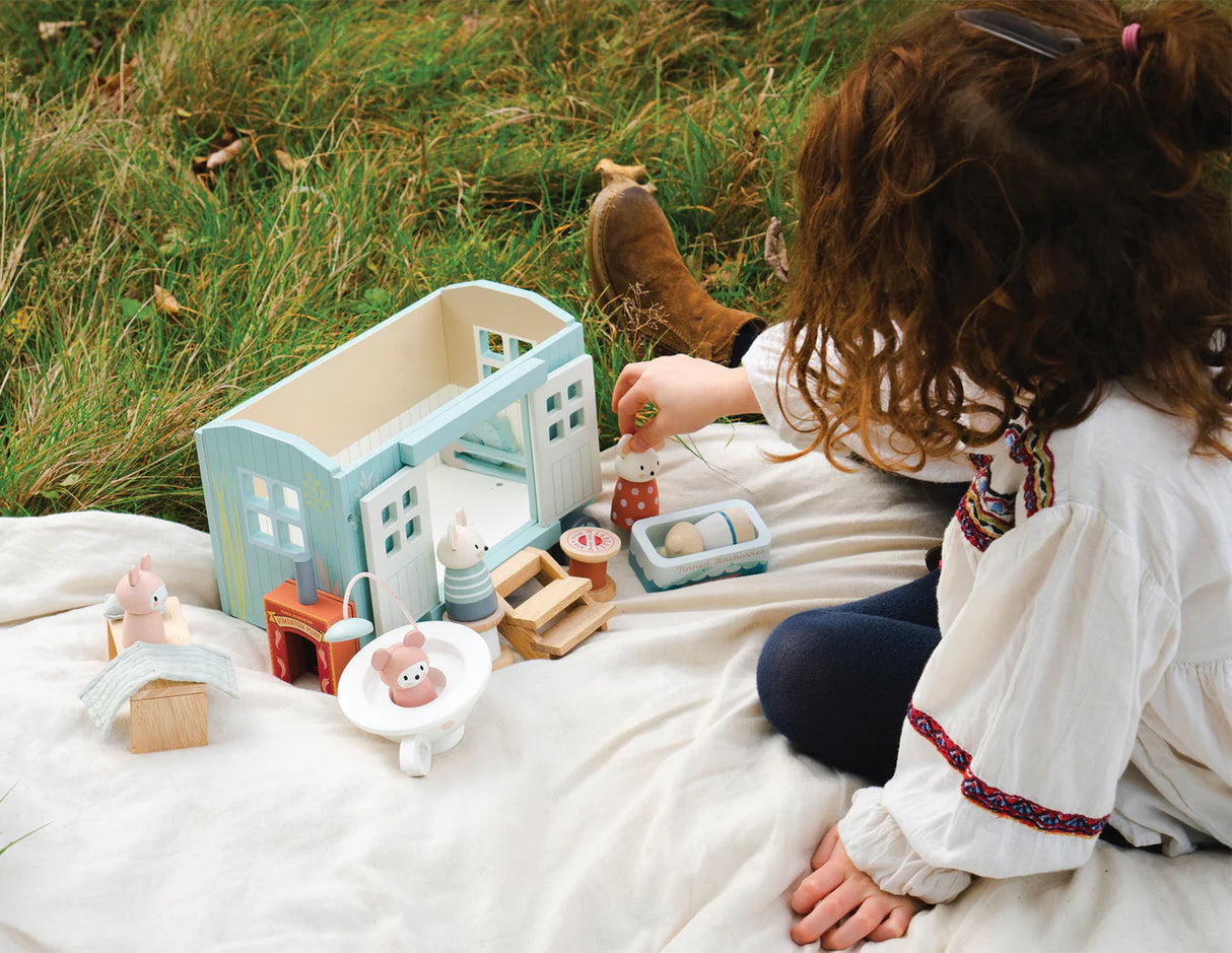 Child playing outdoors with Secret Meadow Shepherd's Hut and miniature furniture on a blanket.