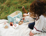 Child playing outdoors with Secret Meadow Shepherd's Hut and miniature furniture on a blanket.