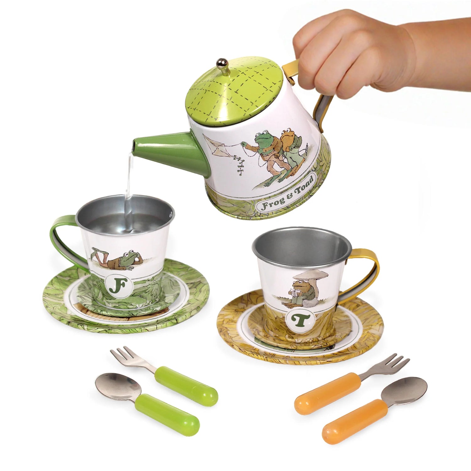 Child’s hand pouring water from Frog and Toad themed tin teapot into matching cups with forks and spoons on white background