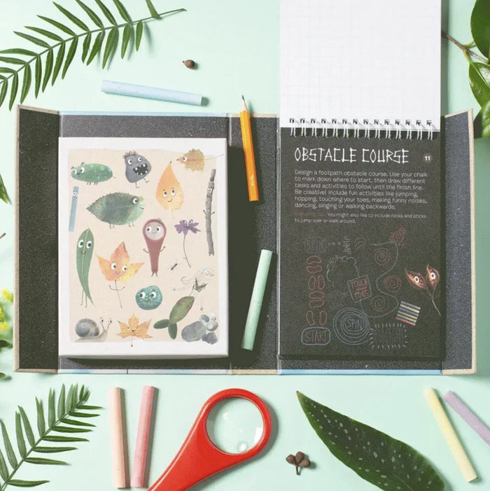 Open sketchbook with whimsical creature drawings colored pencils and a red magnifying glass on a mint green background