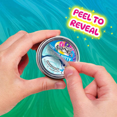 Hands peeling label off a tin of Treasure Reveal Thinking Putty to uncover a hidden design inside