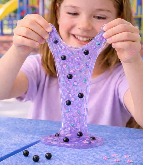 Ooey Gooey Slime Surprise purple glitter slime stretched by a smiling child
