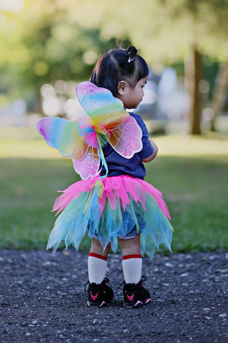 Child wearing Neon Rainbow Skirt Wings & Wand Set with colorful tutu and rainbow wings outdoors.