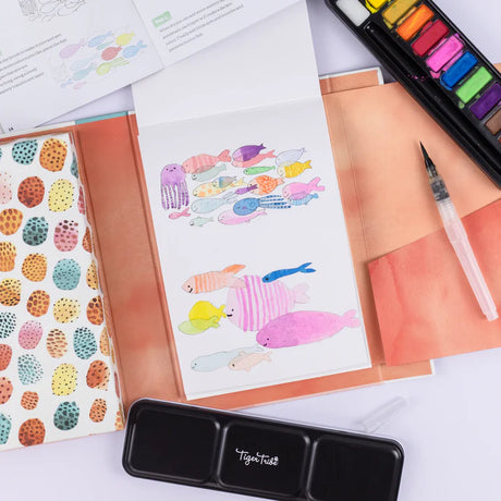 How to Paint | Watercolor Animals set showing colorful fish painting, watercolor palette, and water brush on table.