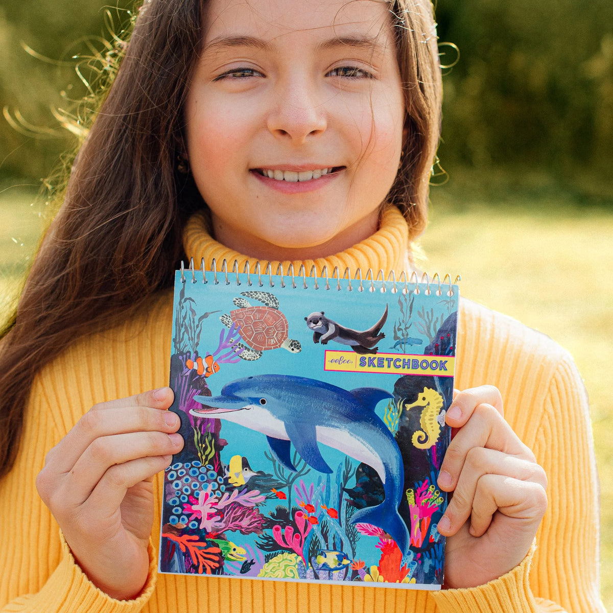 Square Sketchbook | Sea Life held by a smiling child featuring colorful dolphins sea turtles seahorses and coral