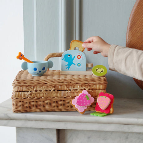 Child playing with Kitten's Breakfast wooden toy set with toast, jams, and a blue cat cup on wicker basket.