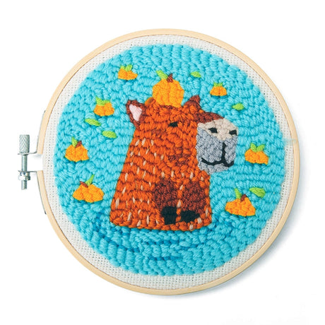 Punch needle embroidery of an orange alpaca with a pumpkin on its head on bright blue fabric background