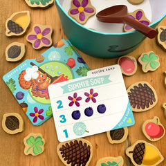 Summer soup recipe card with a colorful bowl, spoon, flowers, berries, and wooden food pieces on a table