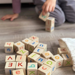 Child playing with colorful wooden alphabet blocks spilled from a white drawstring bag on the floor