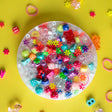 Colorful beads and charms trapped inside a PickMe Pad on a bright yellow background with scattered small objects.