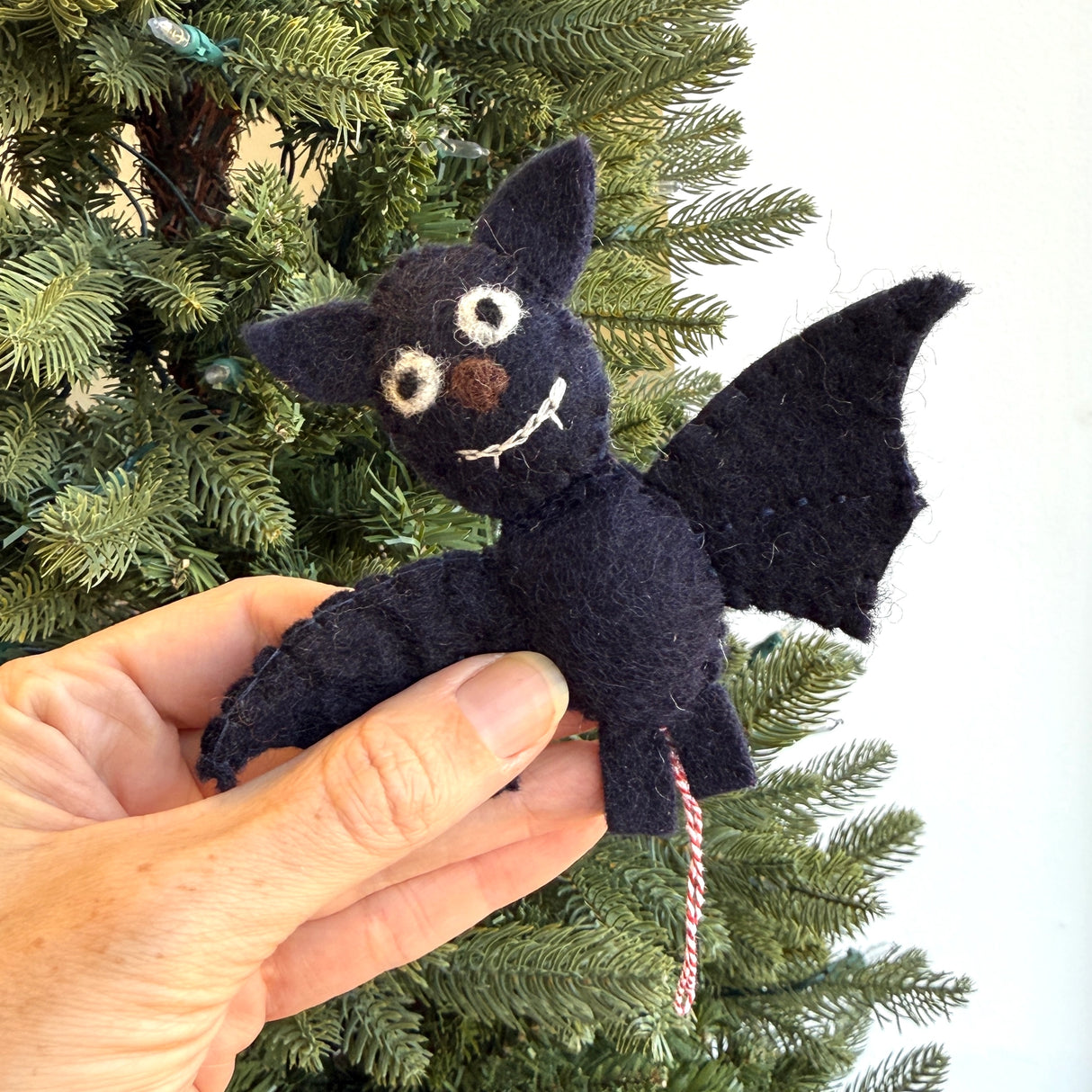 Handmade black felt bat ornament with white eyes and smile hanging on a Christmas tree branch