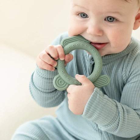 Baby holding a green silicone frog-shaped teether rattle designed to soothe and engage little fingers and gums.