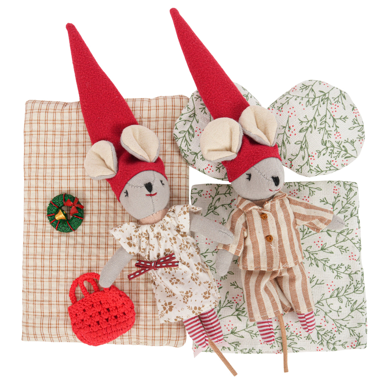 Two whimsical Christmas mice dolls wearing red hats lying on patterned blankets with a small decorative wreath and red bag nearby