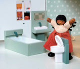 Miniature dollhouse bathroom set with bathtub, sink, toilet, and a doll with black hair and red skirt