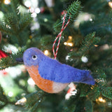 Handmade felt bird ornament in blue and orange wool hanging on a Christmas tree branch with lights.