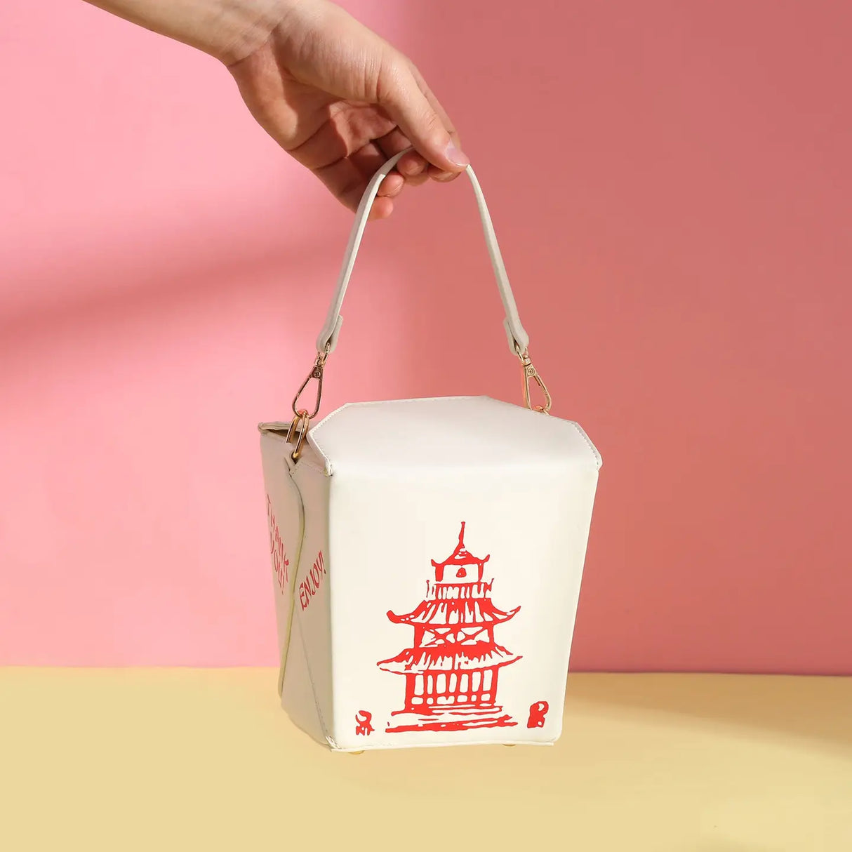 Hand holding the white Handbag | Takeout Box with red pagoda design against a pink background