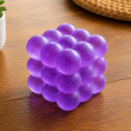 Feelzies Slow Flow Bubble Cube in purple with rounded bubble shapes on a wooden table