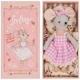Soft gray plush mouse wearing pink check dress and bow, lying in box with fabric cushion background