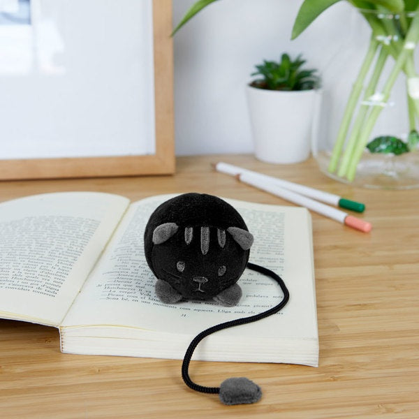 Soft black fluffy animal bookmark shaped like a cat placed on an open book on a wooden table
