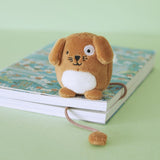 Small fluffy dog-shaped bookmark resting on a book with a patterned cover on a green surface