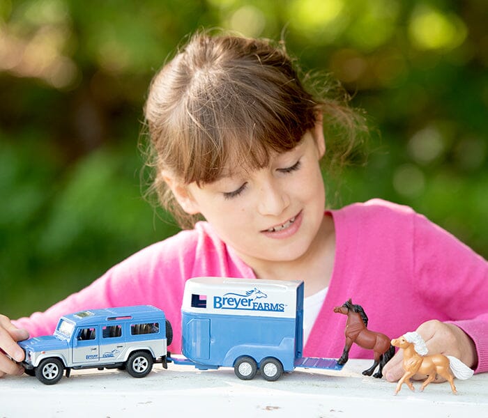 Girl playing with a blue die-cast Land Rover and Breyer Farms two-horse trailer with loading ramp and toy horses