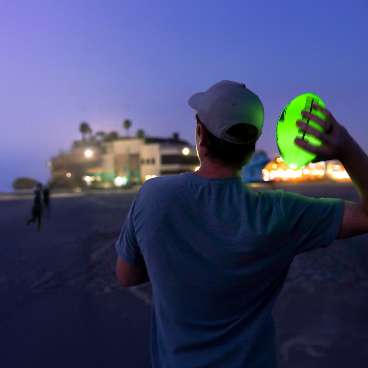 Youth holding glowing football ready to throw at dusk on the beach with blurred lights in background