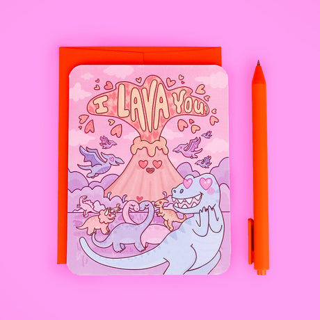 Cute dinosaur themed greeting card with I LAVA You volcano and matching orange envelope and pen on pink background