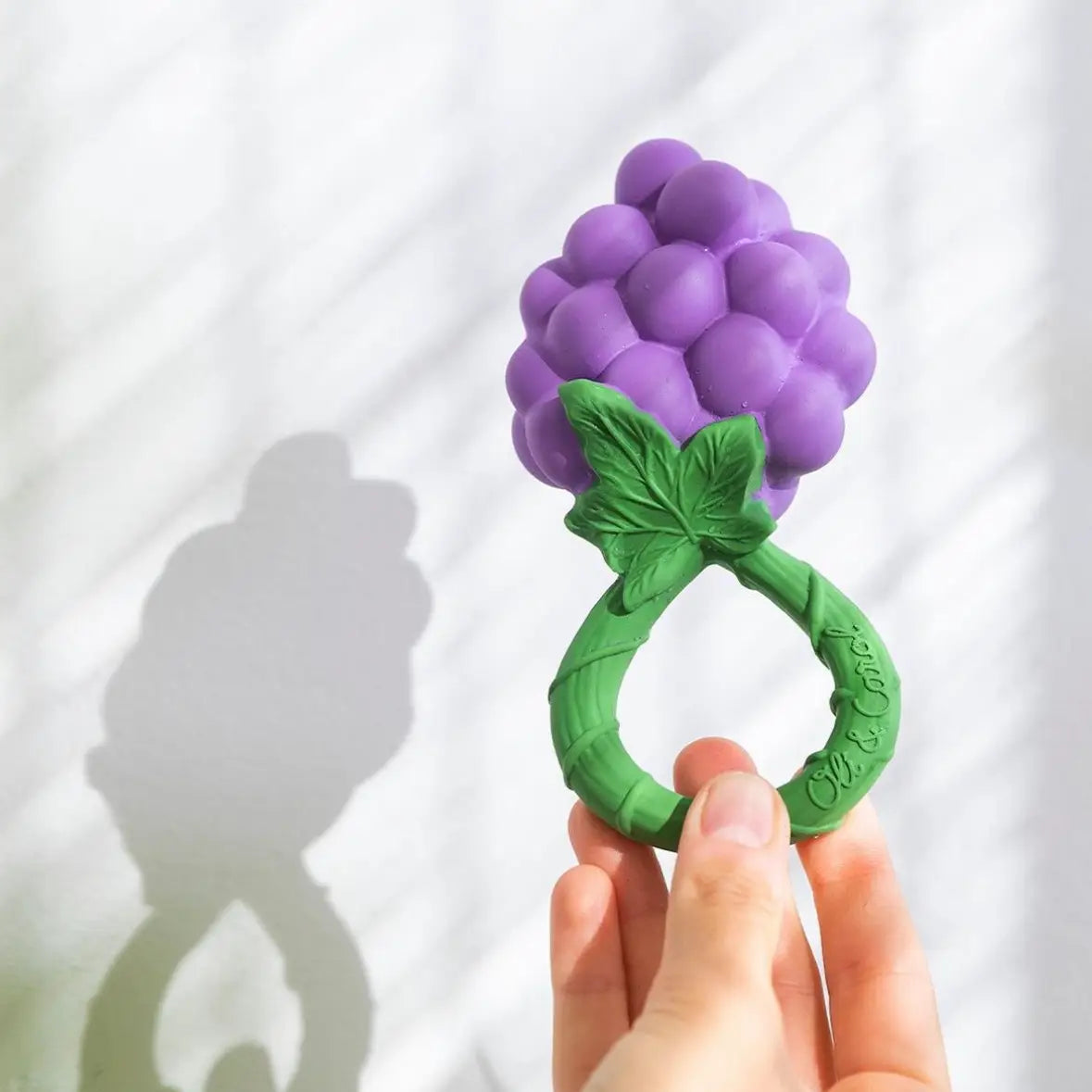 Handheld grape-shaped natural rubber baby rattle and teether with textured green leaf handle against light background