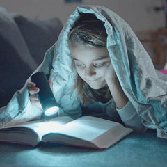 Child reading a book under a blanket with a flashlight shining on the pages