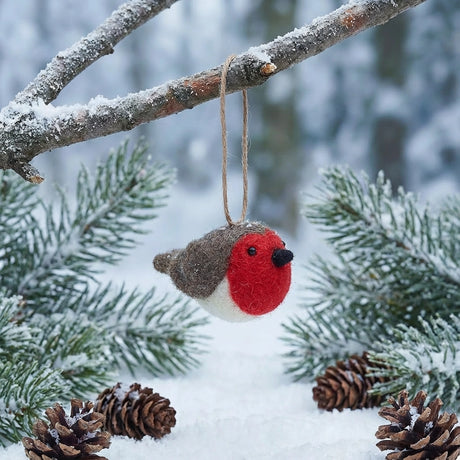 Handcrafted felt robin ornament with vibrant red breast hanging on snowy pine branch with pine cones below