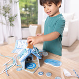 Child playing with a blue wooden gingerbread house play set with reusable decorations on a bright table indoors