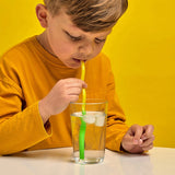 Young boy in orange shirt drinking ice water through a flexible yellow and green curly straw against a yellow backdrop