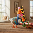 Colorful felt dodo ornament wearing a neon orange hat and pink glasses holding a wreath on a wooden table with festive decor