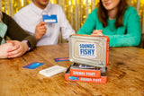 Sounds Fishy Travel Tin game on a table with players holding cards