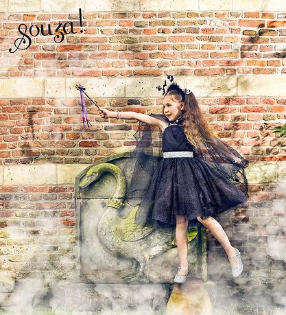 Young girl dressed as a witch holding a sparkling spider web wand with black, purple, and silver ribbons outdoors