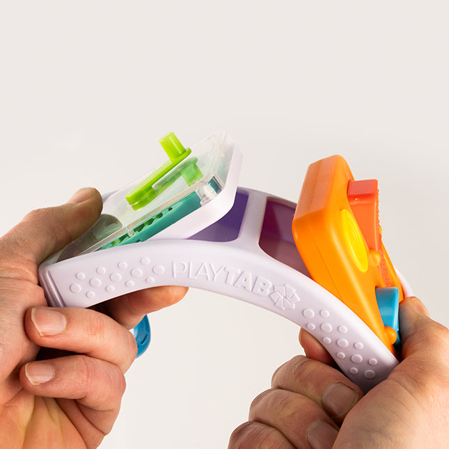 Hands holding flexible PlayTab Go activity board with two colorful sensory tiles attached