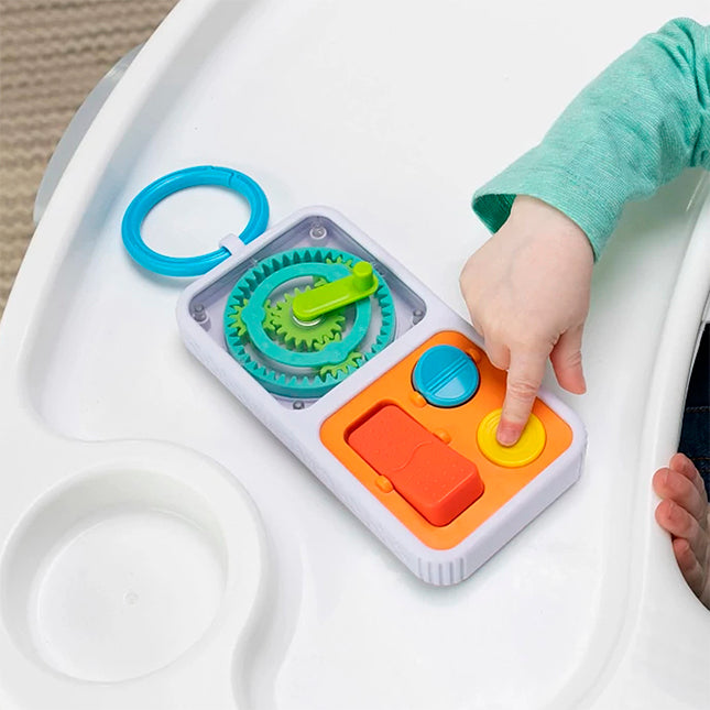 Child playing with a colorful PlayTab Go sensory tile toy on a white tray surface with clip attached.