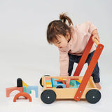 Toddler playing with a wooden block trolley filled with colorful building blocks, pushing it by the handle.